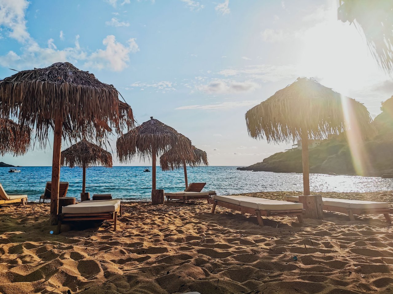 The beach in Ios, Greece with golden sand, blue water, sunny skies and beach umbrellas.